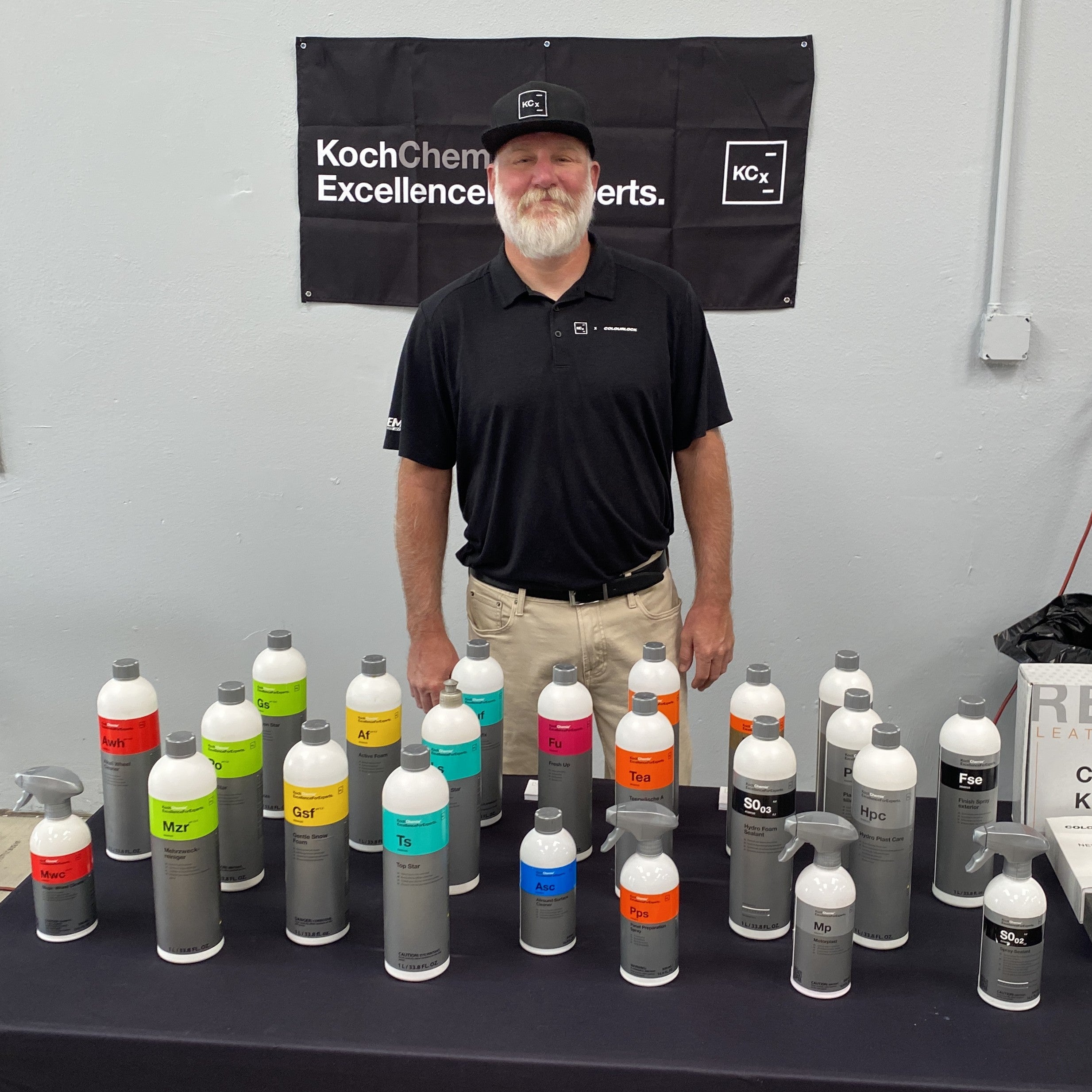 Man standing behind a table with various bottles and a Koch Chem Excellence banner in the background.