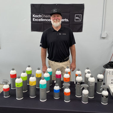 Man standing behind a table with various bottles and a Koch Chem Excellence banner in the background.